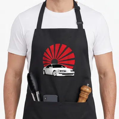 Tablier de cuisine noir avec illustration d'une voiture blanche sur fond de soleil levant rouge rayonnant.