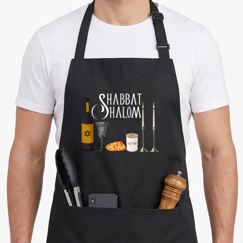 Tablier de cuisine noir avec illustration Shabbat Shalom, Vin, Challah et Bougies rituelles en style graphique coloré.
