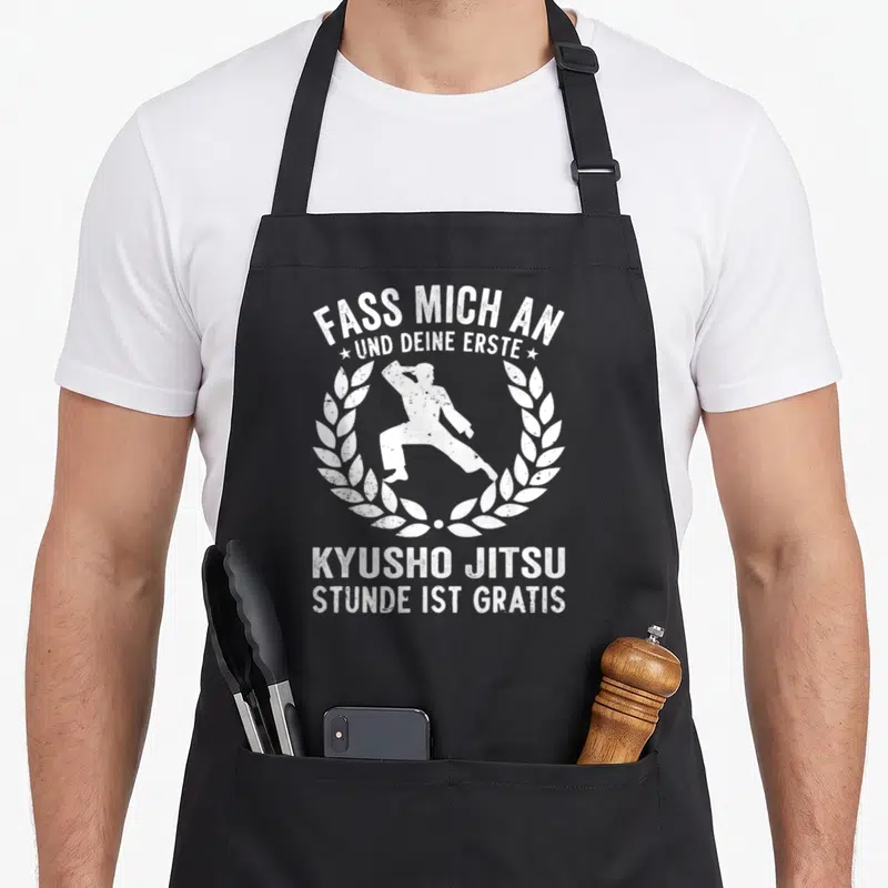 Tablier de cuisine noir avec silhouette martiale et inscription allemande fass mich an kyusho jitsu gratis entourée de couronnes de laurel.
