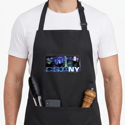 Tablier de cuisine noir avec logo CSI: NY et skyline nocturne de New York en arrière-plan.