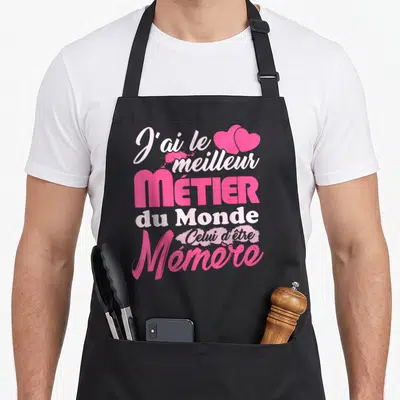 Tablier de cuisine noir avec inscription rose J'ai le meilleur métier du monde celui d'être Mémère et deux cœurs en haut à droite.