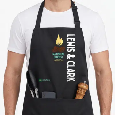 Tablier de cuisine noir avec logo Lewis & Clark National Forest Montana et illustration de feu de camp.