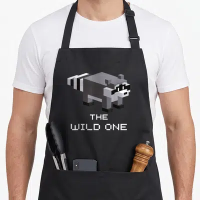 Tablier de cuisine noir avec illustration pixelisée d'un raton laveur et le texte The Wild One en blanc.