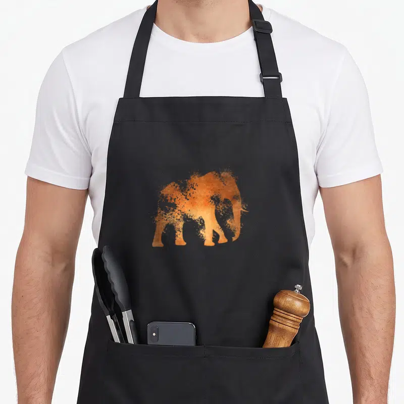 Tablier de cuisine noir avec silhouette d'éléphant orange effet poussière artisticque au centre.