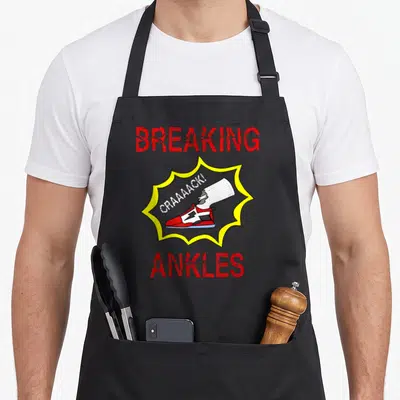 Tablier de cuisine noir avec illustration de chaussure rouge et texte Breaking Ankles en lettres rouges.