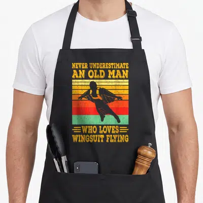 Tablier de cuisine noir avec silhouette wingsuit sur fond de bandes colorées vintage et texte jaune.