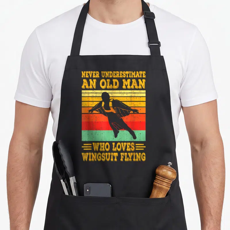 Tablier de cuisine noir avec silhouette wingsuit sur fond de bandes colorées vintage et texte jaune.