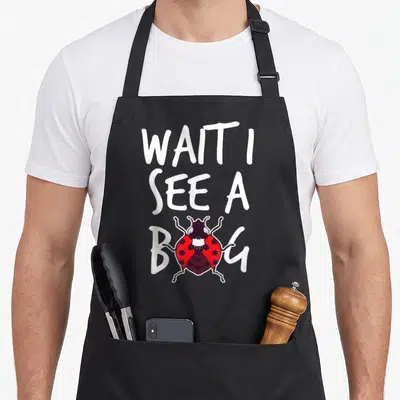 Tablier de cuisine noir avec l'inscription Attends je vois un bug et une coccinelle rouge.