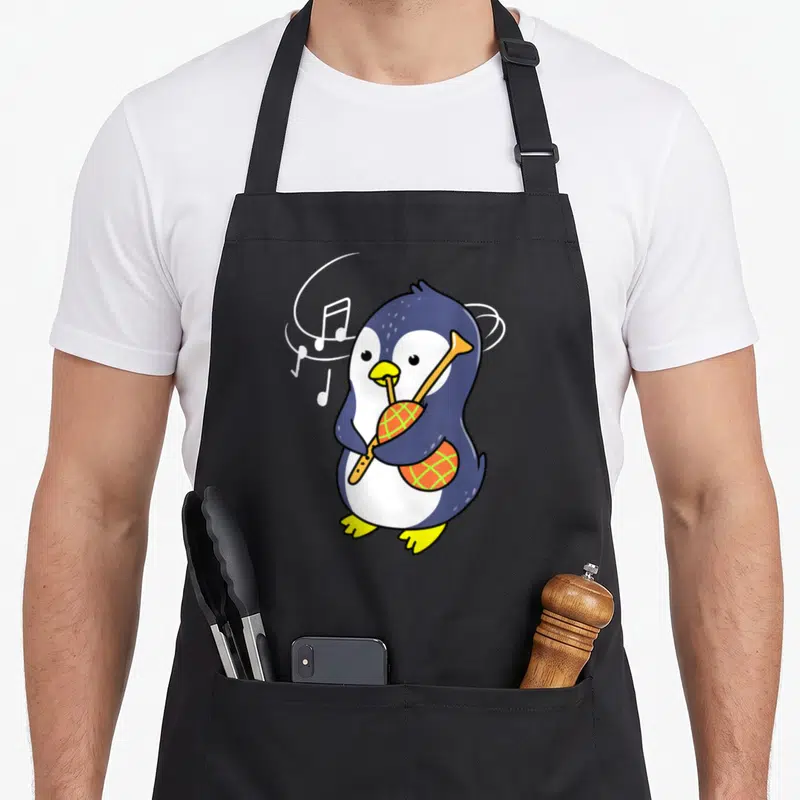 Tablier de cuisine noir avec un pingouin jouant de la cornemuse et des notes de musique flottantes.