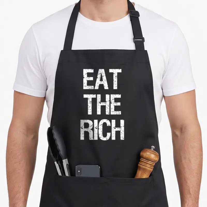 Tablier de cuisine noir avec l'inscription blanche « Eat The Rich » en lettres capitales texturées au centre du devant.