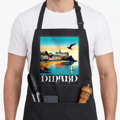 Tablier de cuisine noir avec illustration retro de Dinard, plage, voilier et seagull en vol au-dessus des bâtiments colorés.