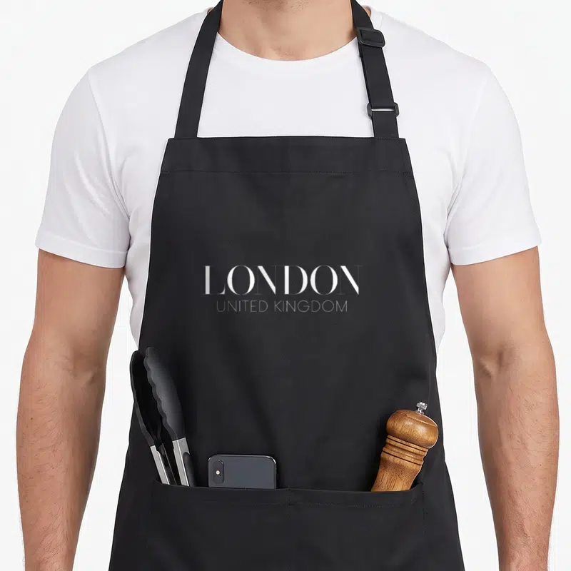 Tablier de cuisine noir avec l'inscription blanche LONDON UNITED KINGROOM en typographie fine et élégante.