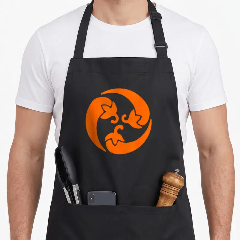 Tablier de cuisine noir avec motif circulaire orange stylisé représentant trois piments entrelacés dans un design graphique moderne.