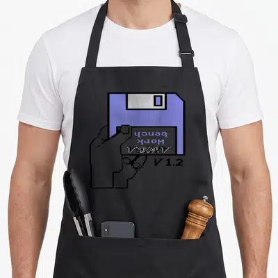 Tablier de cuisine noir avec illustration pixel art d'une main tenant une disquette Amiga Workbench V1.2 bleue et grise.