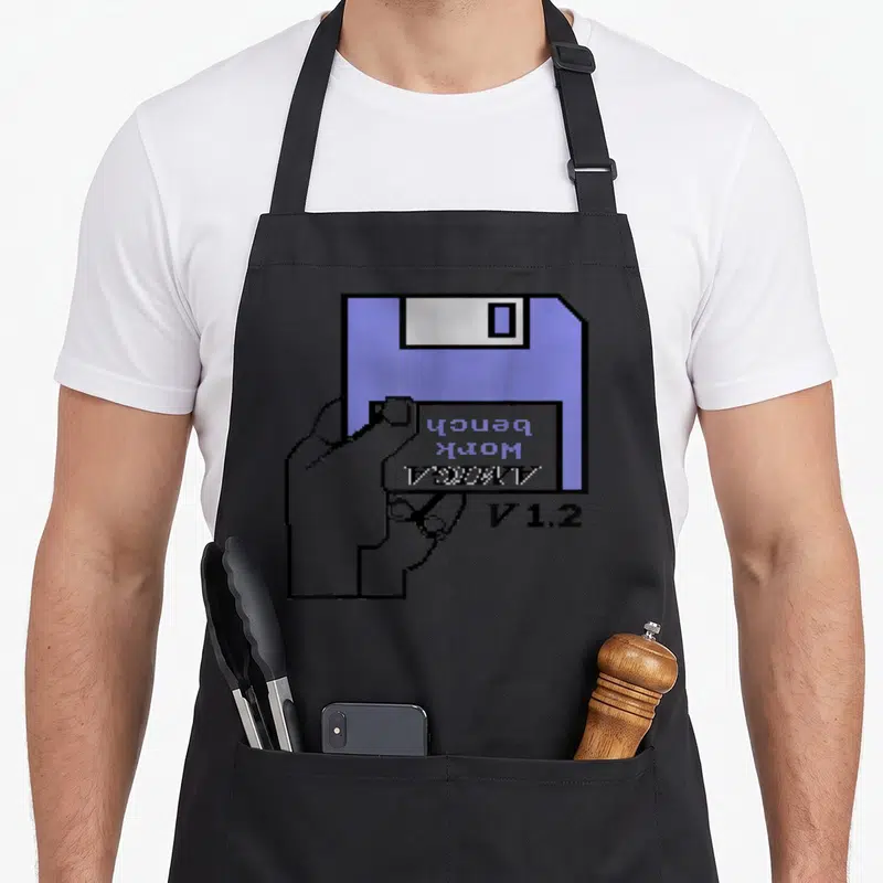 Tablier de cuisine noir avec illustration pixel art d'une main tenant une disquette Amiga Workbench V1.2 bleue et grise.