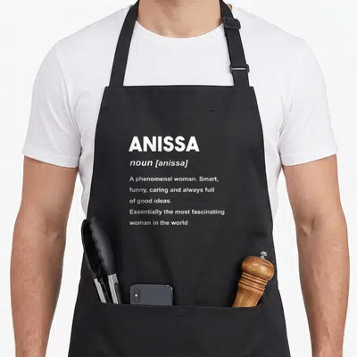 Tablier de cuisine noir avec la définition du nom Anissa en typographie blanche style dictionnaire.