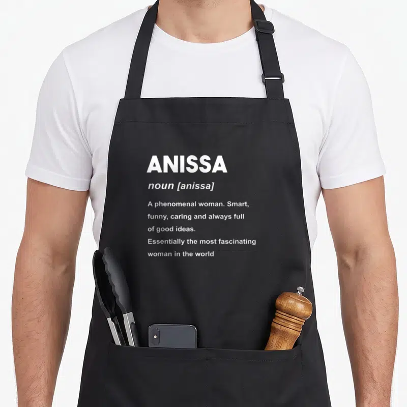 Tablier de cuisine noir avec la définition du nom Anissa en typographie blanche style dictionnaire.