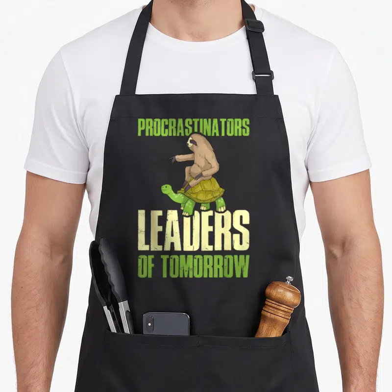 Tablier de cuisine noir avec un slow assis sur une tortue et le texte Procrastinateurs Leaders de demain