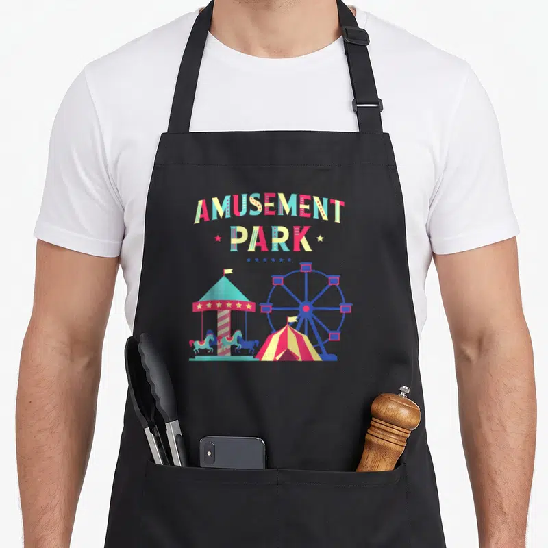 Tablier de cuisine noir avec illustration colorée d'une grande roue, d'un carrousel et d'une tente de cirque sous le texte Amusement Park.