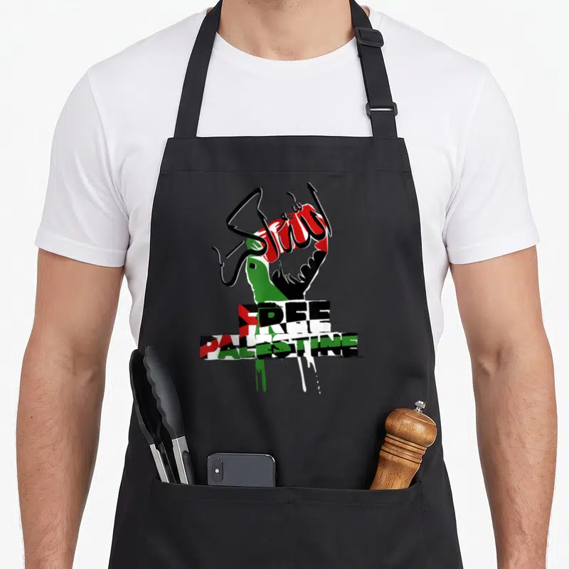 Tablier de cuisine noir orné d'un poing levé aux couleurs palestiniennes et du texte Free Palestine Libre en typographie graffiti.