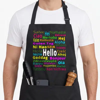 Tablier de cuisine noir avec Hello, Bonjour et d'autres salutations multicolores disposées en nuage typographique.