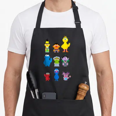 Tablier de cuisine noir avec neuf personnages de dessin animé stylisés en pixel art 8 bits colorés disposés en grille.