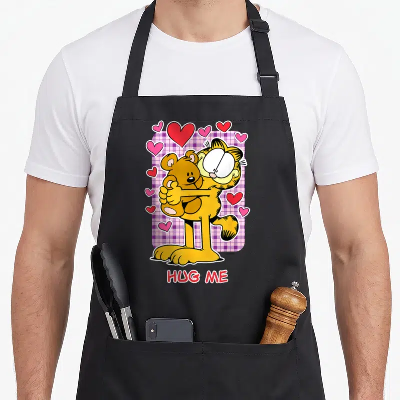 Tablier de cuisine noir avec Garfield serrant un ours en peluche et le texte HUG ME en bas.