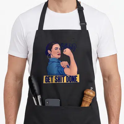 Tablier de cuisine noir avec illustration d'une femme flexant et le texte Bitches Get Shit Done sur fond jaune.