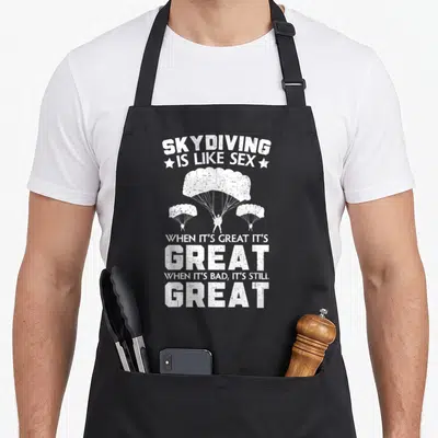 Tablier de cuisine noir avec texte blanc Skydiving is like sex et trois parachutistes illustrés.