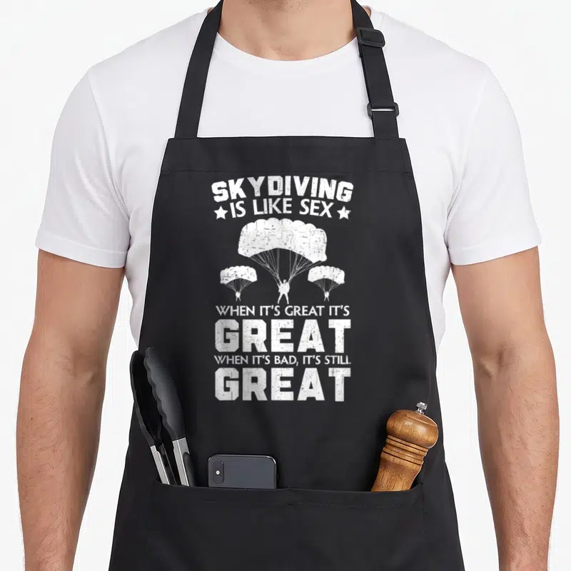 Tablier de cuisine noir avec texte blanc Skydiving is like sex et trois parachutistes illustrés.