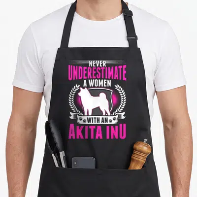 Tablier de cuisine noir avec silhouette blanche d'Akita Inu encadrée de couronnes et texte rose vif.