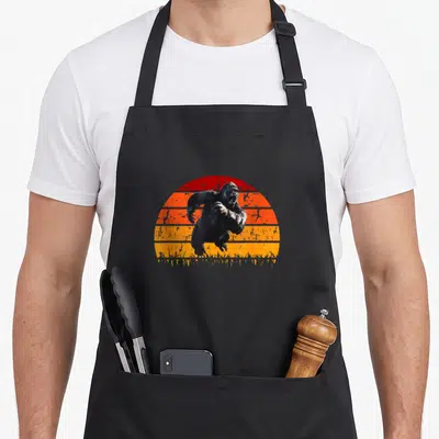 Tablier de cuisine noir avec illustration gorille sautant devant un soleil orange et rouge style vintage