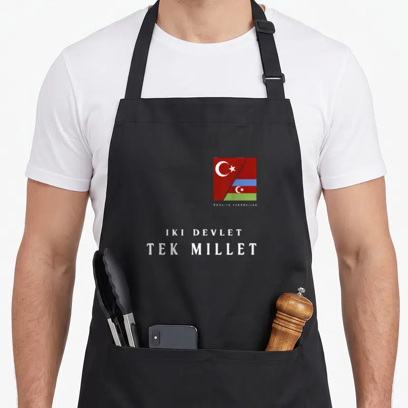 Tablier de cuisine noir avec drapeaux unis et texte blanc Iki Devlet Tek Millet centré sur le devant.