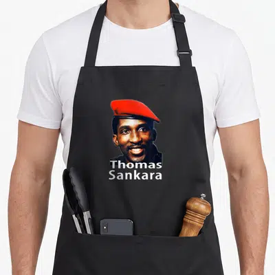 Tablier de cuisine noir avec le portrait souriant de Thomas Sankara coiffé d'une berrette rouge vif.