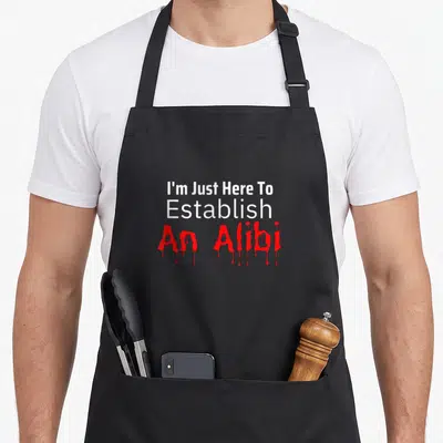 Tablier de cuisine noir avec le texte I'm Just Here To Establish An Alibi en rouge et blanc.