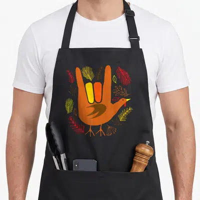 Tablier de cuisine noir avec illustration main orange transformée en dinde et plumes colorées.
