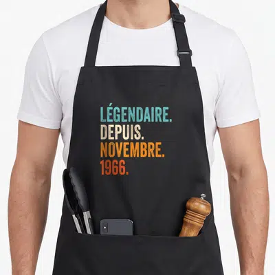 Tablier de cuisine noir avec inscription légendaire depuis novembre 1966 en lettres colorées vintage.