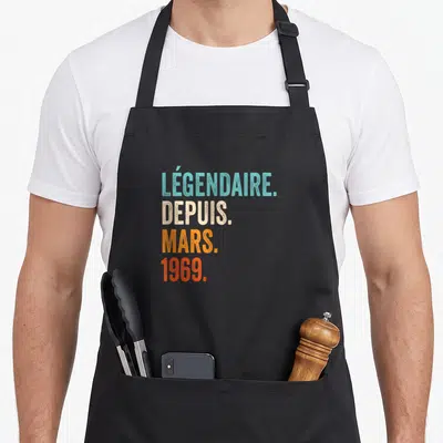Tablier de cuisine noir avec l'inscription Légendaire Depuis Mars 1969 en lettres colorées et style vintage.