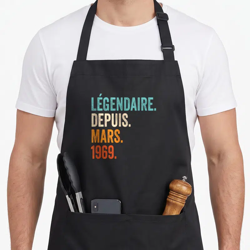 Tablier de cuisine noir avec l'inscription Légendaire Depuis Mars 1969 en lettres colorées et style vintage.