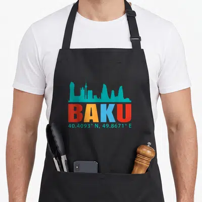 Tablier de cuisine noir avec skyline turquoise et le mot BAKU aux lettres multicolores surmontant des coordonnées géographiques.