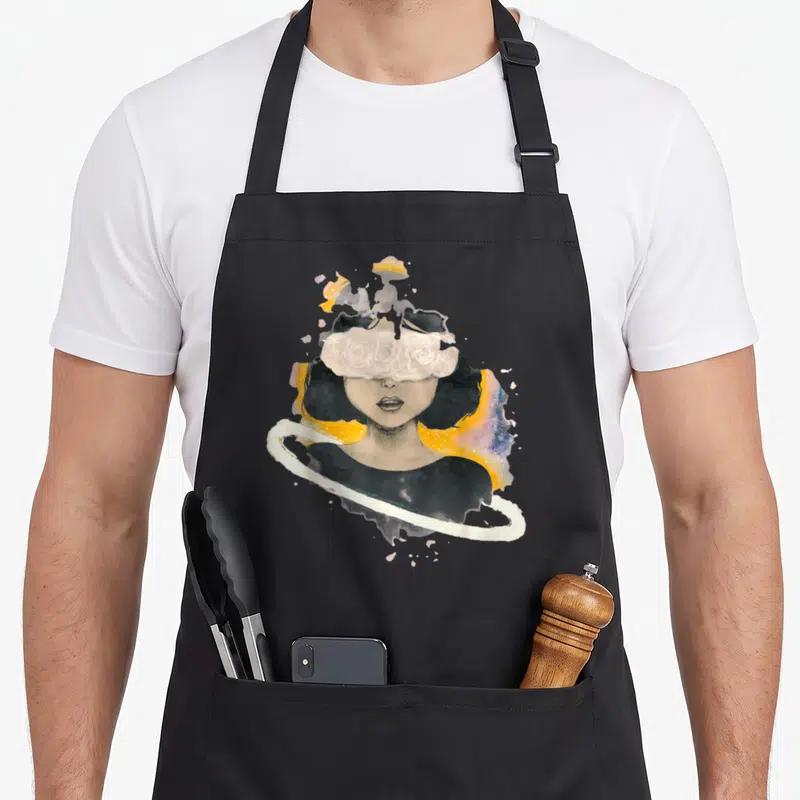 Tablier de cuisine noir avec illustration d'une femme aux roses blanches sur les yeux et halo cosmique jaune.