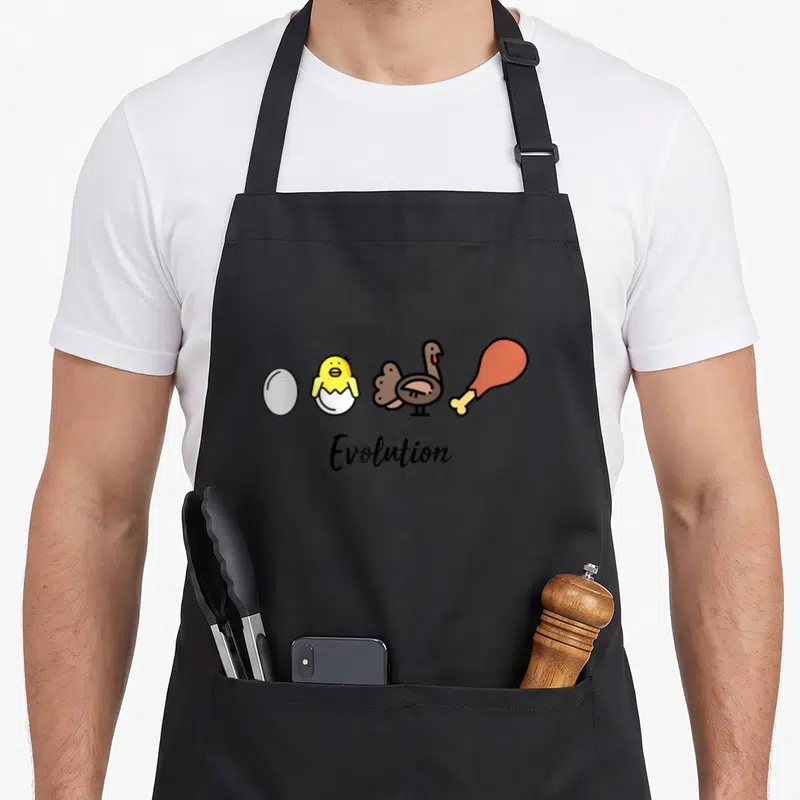 Tablier de cuisine noir avec illustration d'un œuf, poussin, dinde et jamon d'avatar sous le mot Evolution.