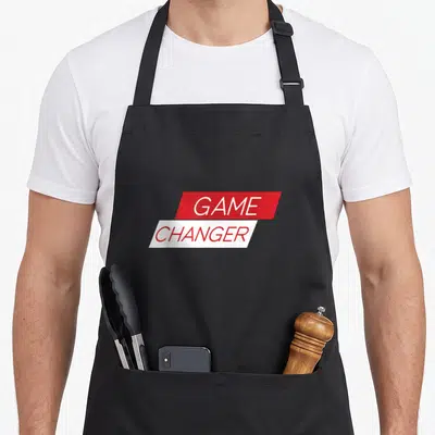 Tablier de cuisine noir avec un logo rectangulaire rouge et blanc portant l'inscription Game Changer en lettres capitales.