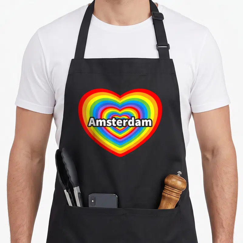 Tablier de cuisine noir avec un grand cœur multicolore en arcs-en-ciel et le texte Amsterdam au centre.