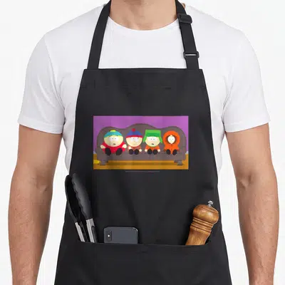 Tablier de cuisine noir avec quatre personnages animés assis côte à côte sur un canapé gris devant un mur violet.