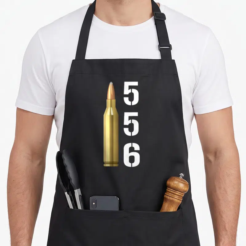Tablier de cuisine noir avec illustration d'une cartouche 556 dorée et texte blanc vertical 556 à côté.