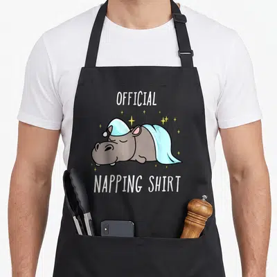 Tablier de cuisine noir avec un hippopotame endormi en pyjama bleu et les mots Official Napping Shirt.