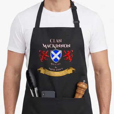 Tablier de cuisine noir avec blason clan Mackinnon, lions rouges et inscription Roguery and Mischief since the middle ages sur banderole dorée.