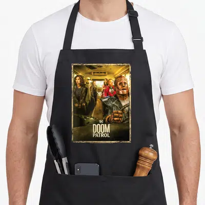 Tablier de cuisine noir avec illustration du bus et personnages Doom Patrol en couleur dorée.