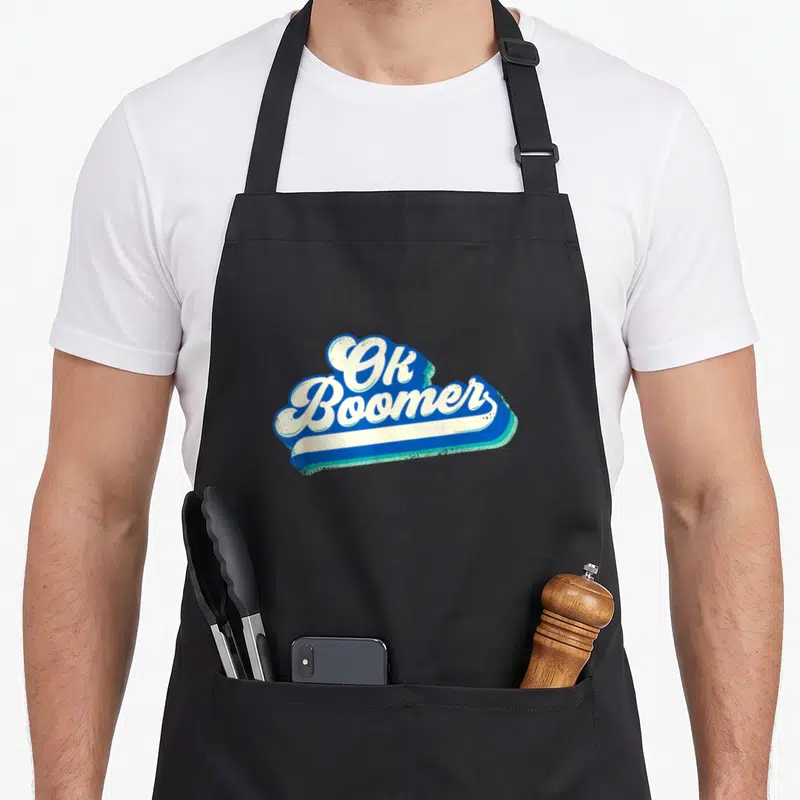 Tablier de cuisine noir avec le logo Ok Boomer en lettres blanches sur fond bleu vintage.